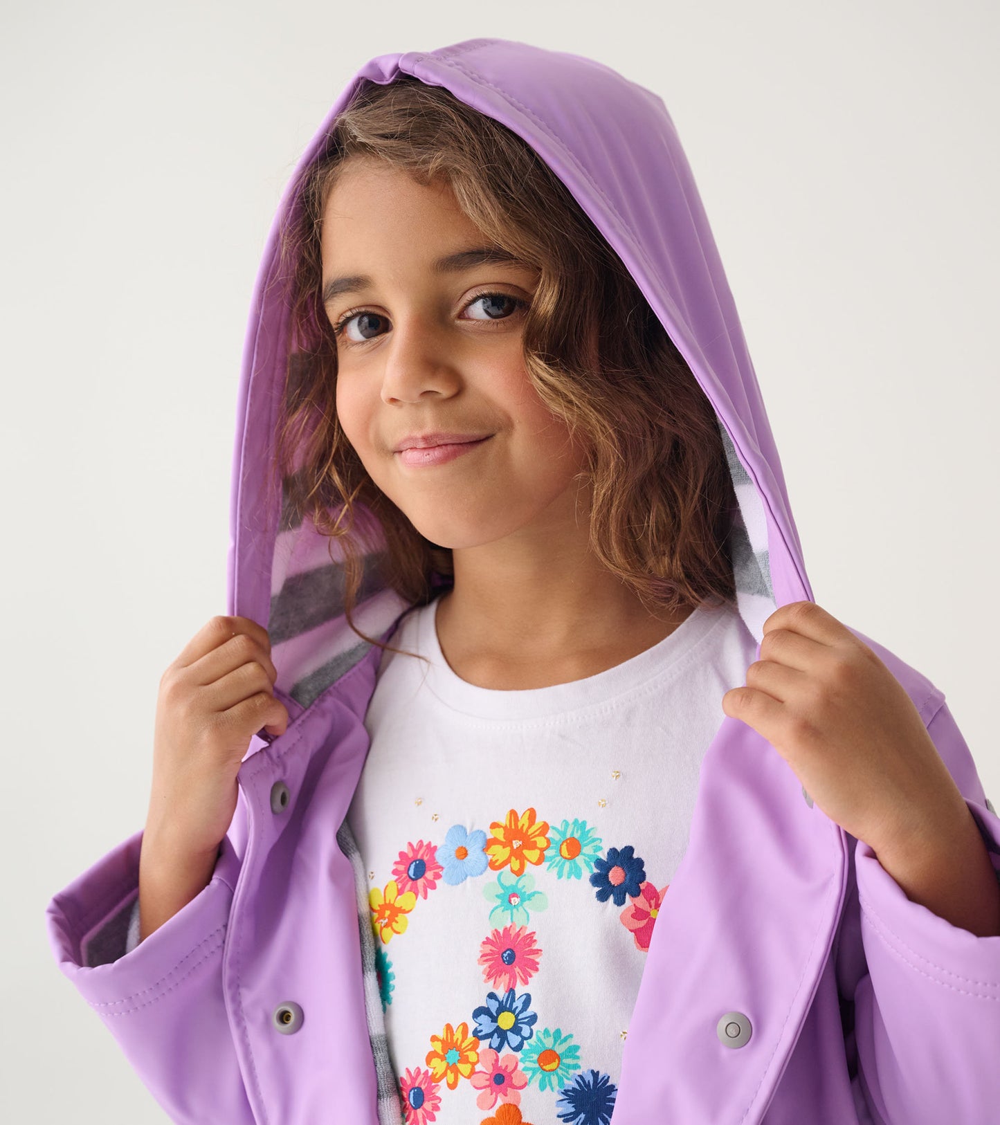 Lilac button-up rain jacket with a hood, featuring a striped lining, worn by a girl holding the jacket open.