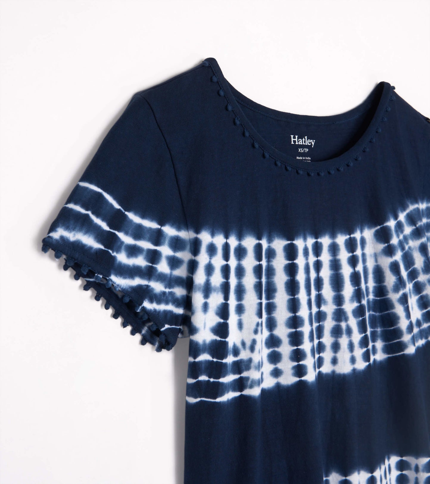 Navy blue tie-dye tee with white patterns and pom-pom trim on sleeves, featuring a round neckline.