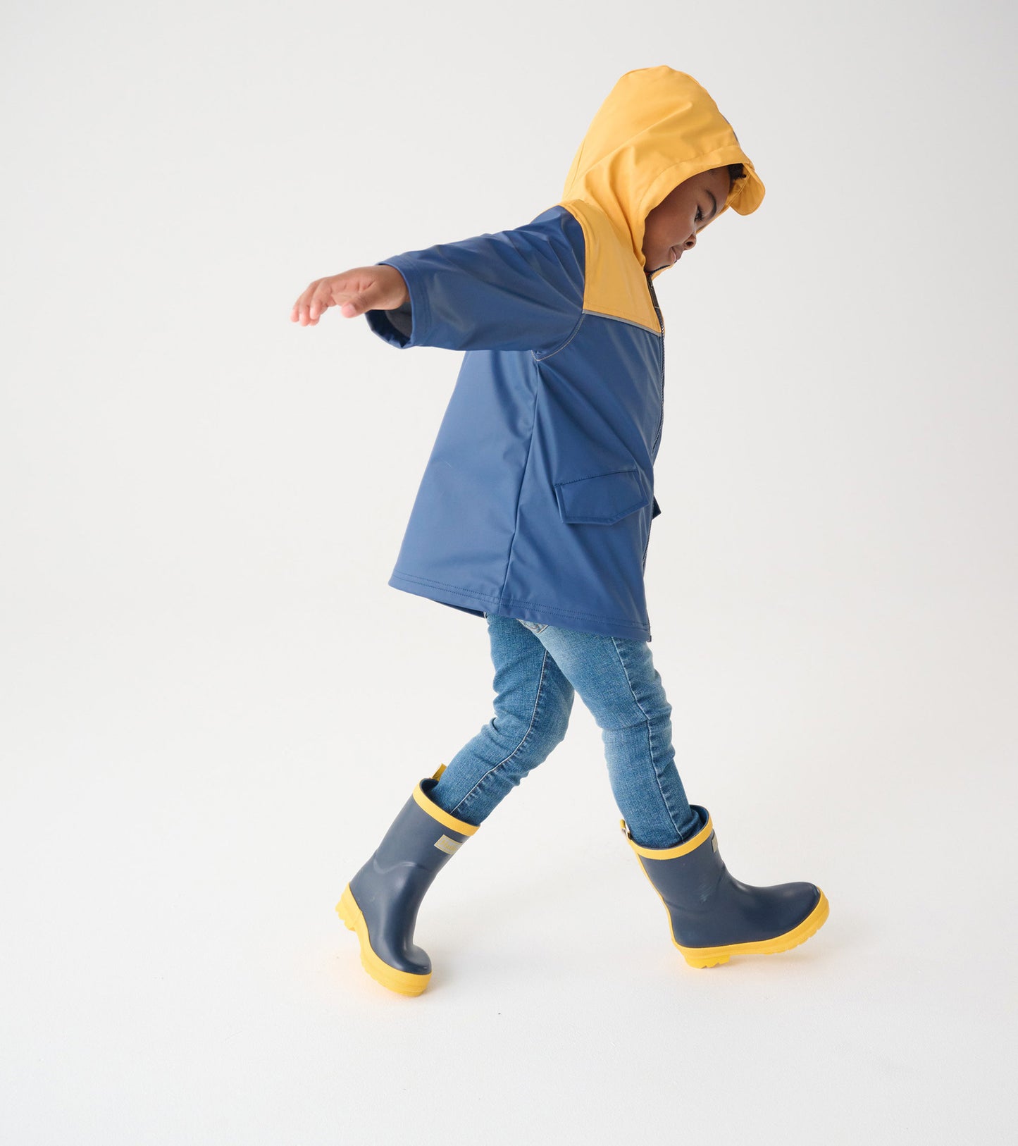 Yellow and navy zip-up rain jacket with a hood, worn by a child, paired with blue jeans and gray rain boots.