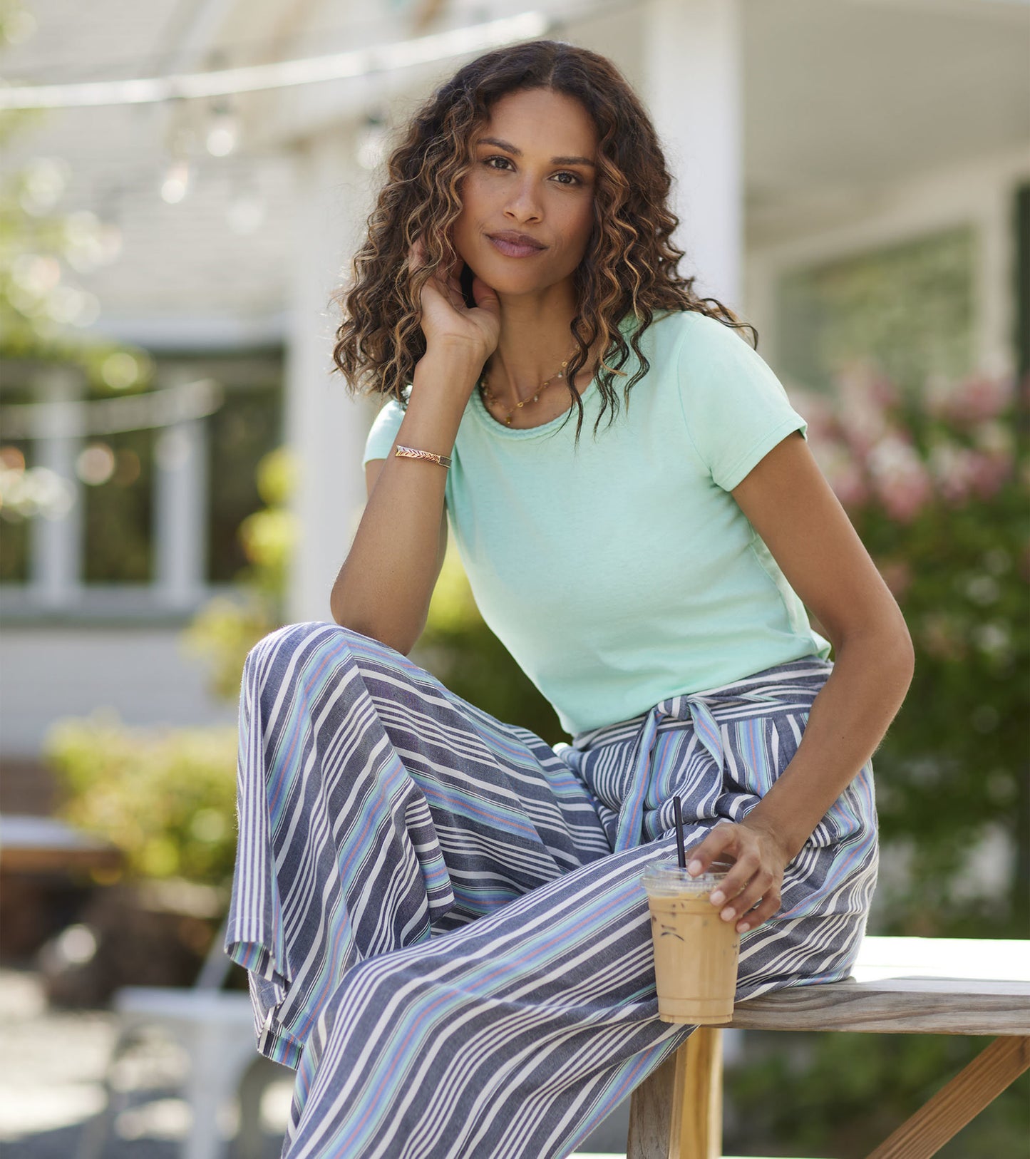 Ice green braided neck tee paired with striped wide-leg pants, worn by a woman sitting outdoors with a drink.