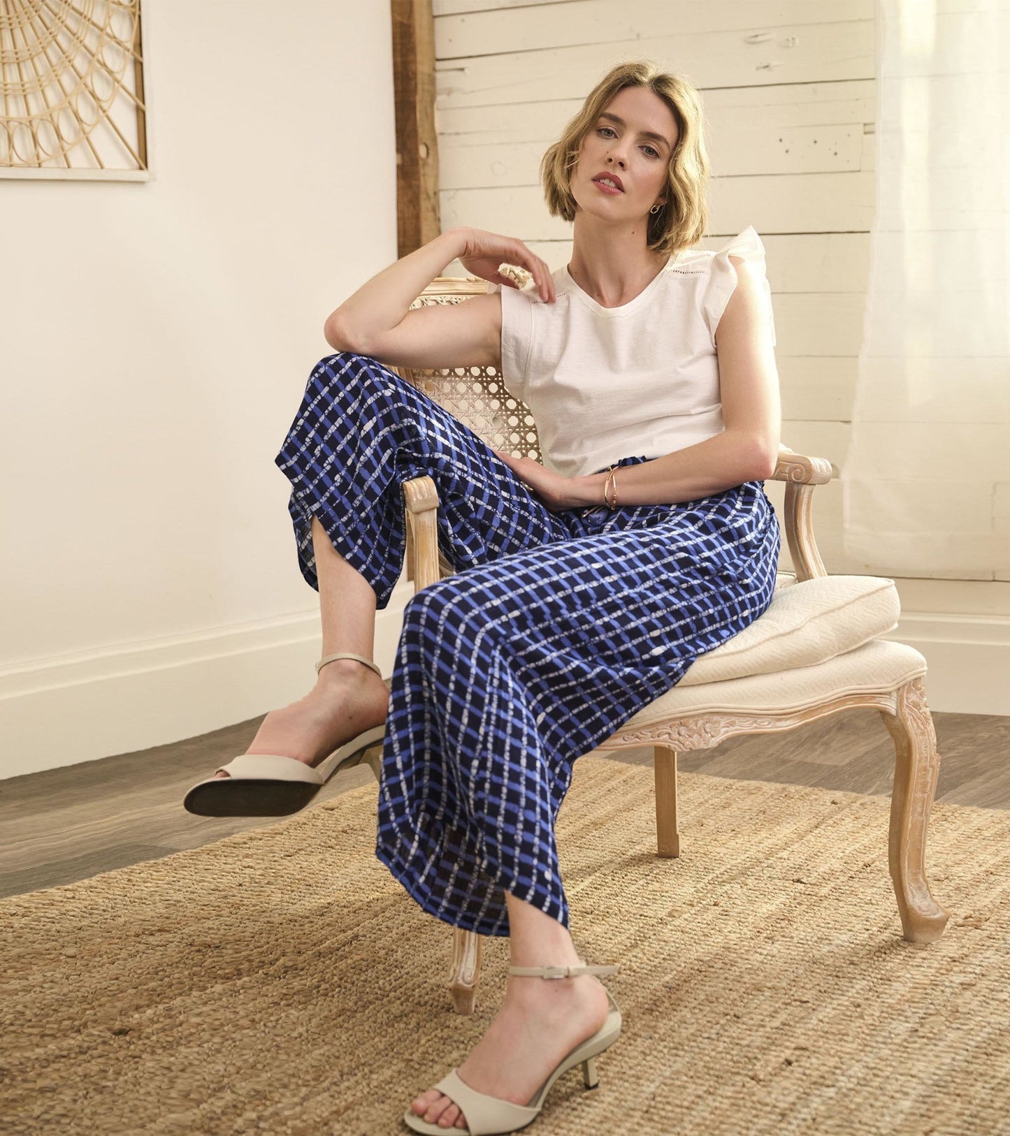 Blue plaid wide-leg pants with side slits, styled with a white top and beige heels, seated on a chair.