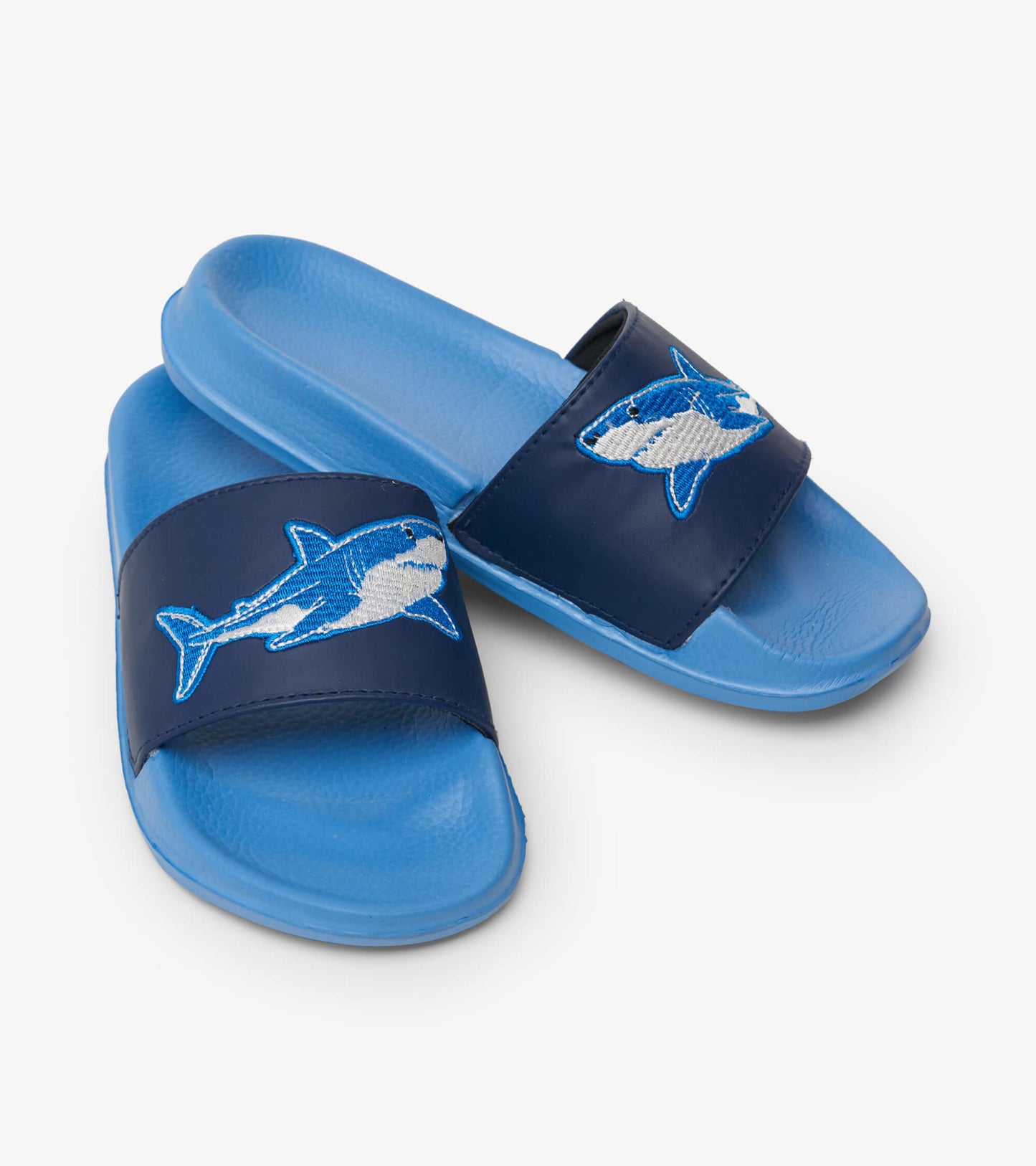 Blue toddler slides featuring a navy strap with an embroidered shark design and a textured blue footbed.