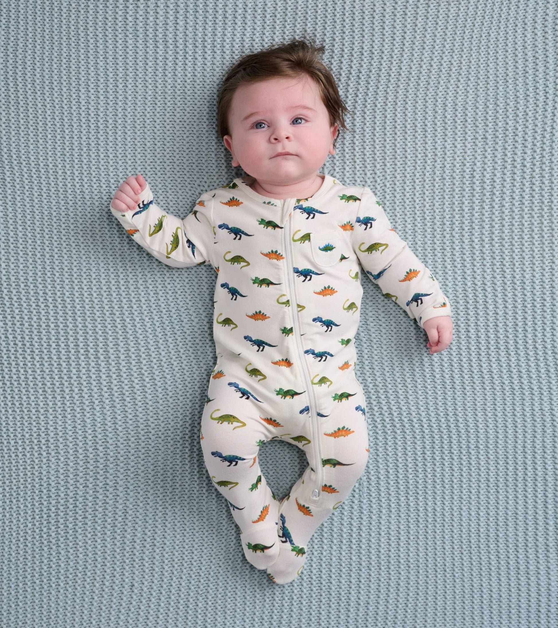 Cream footed sleeper featuring colorful dinosaur prints, designed for infants, with a front zipper closure.
