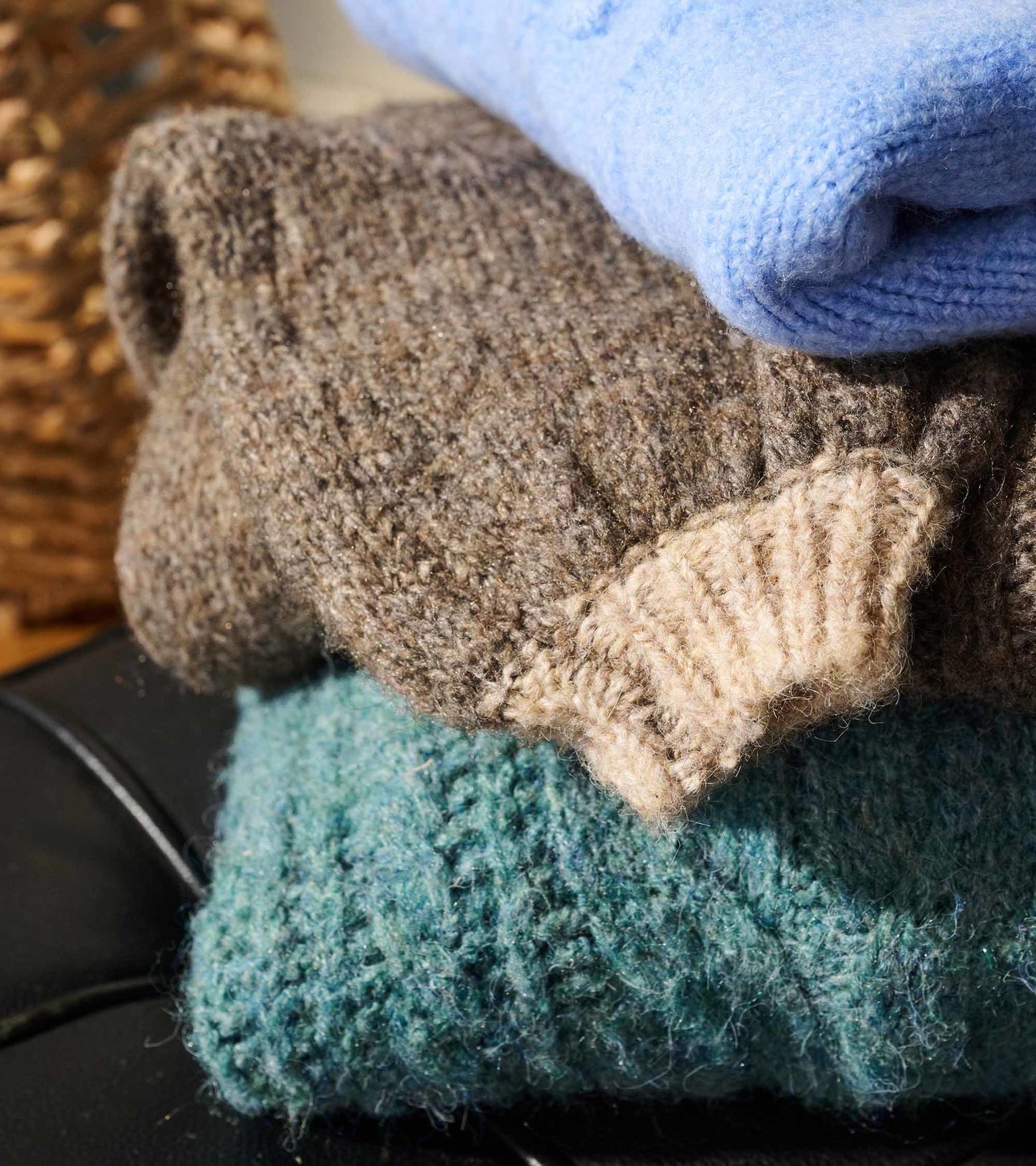 Stack of three sweaters in brown, blue, and teal, showcasing textured knit patterns and ribbed cuffs.