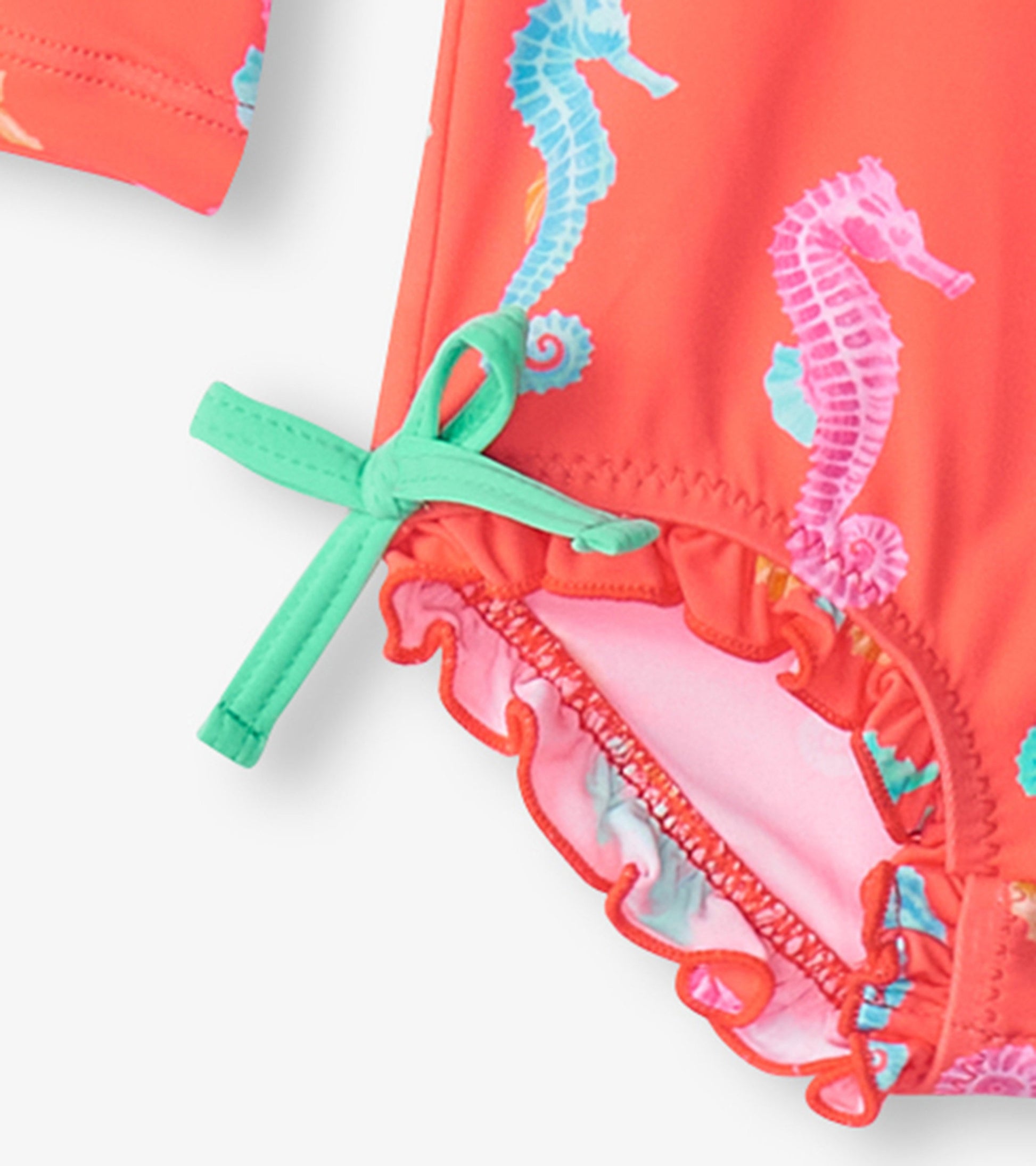Coral rashguard swimsuit featuring colorful seahorse prints and a ruffled hem with a mint green tie detail.