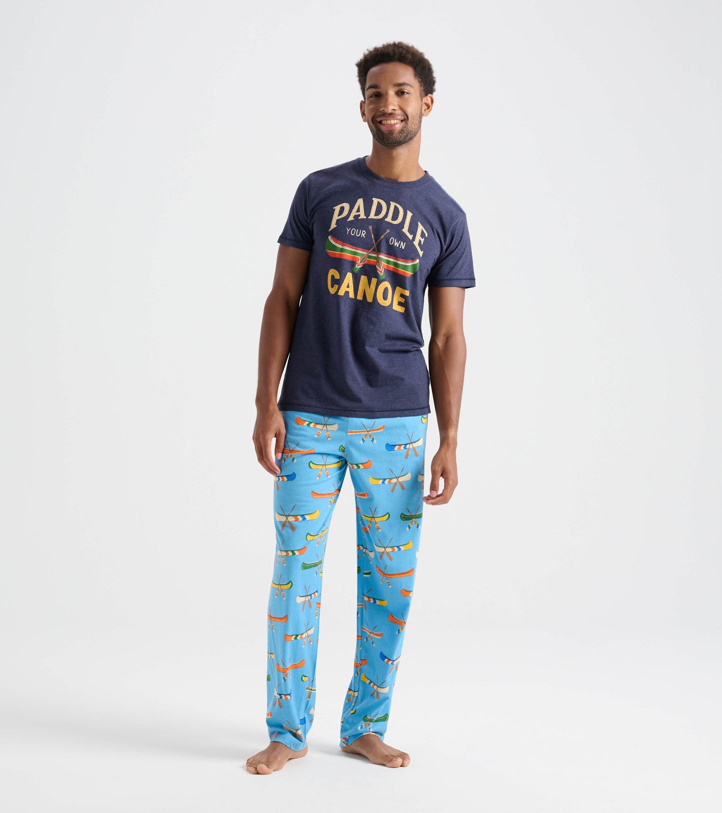 Light blue cotton pajama pants featuring a colorful canoe pattern, worn by a man standing barefoot.