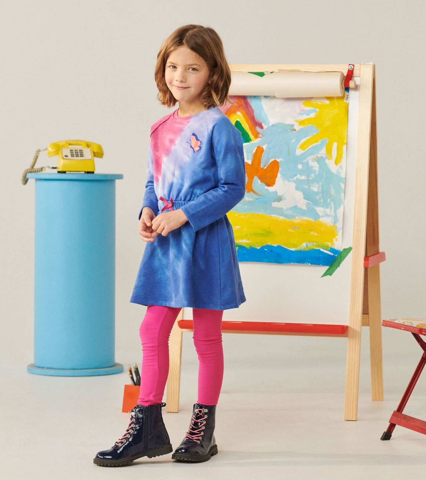 Tie-dye dress with cinched waist, featuring blue and pink hues, paired with pink leggings and black lace-up boots.