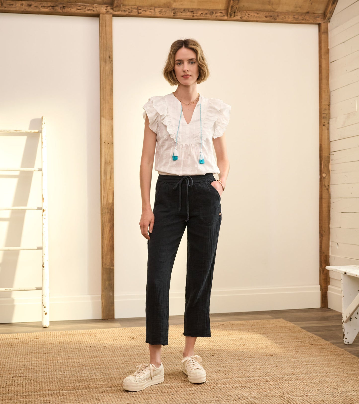 Lightweight white blouse with ruffled sleeves paired with dark plaid pants, styled with casual sneakers.