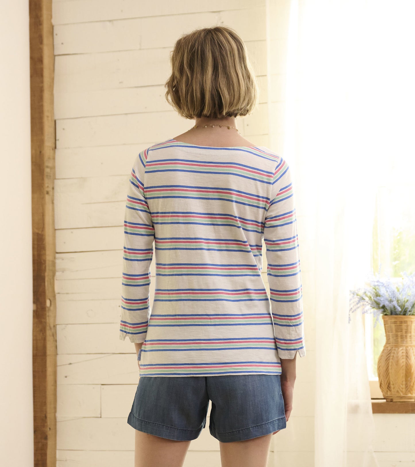 Long-sleeve top featuring a light gray base with colorful horizontal stripes, styled with denim shorts.