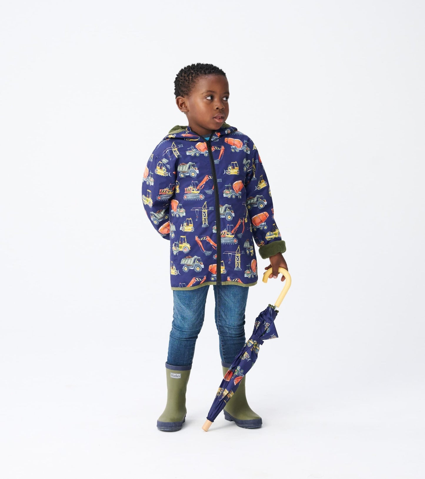 Navy microfiber jacket with construction truck patterns, paired with blue jeans and green rain boots, held with an umbrella.