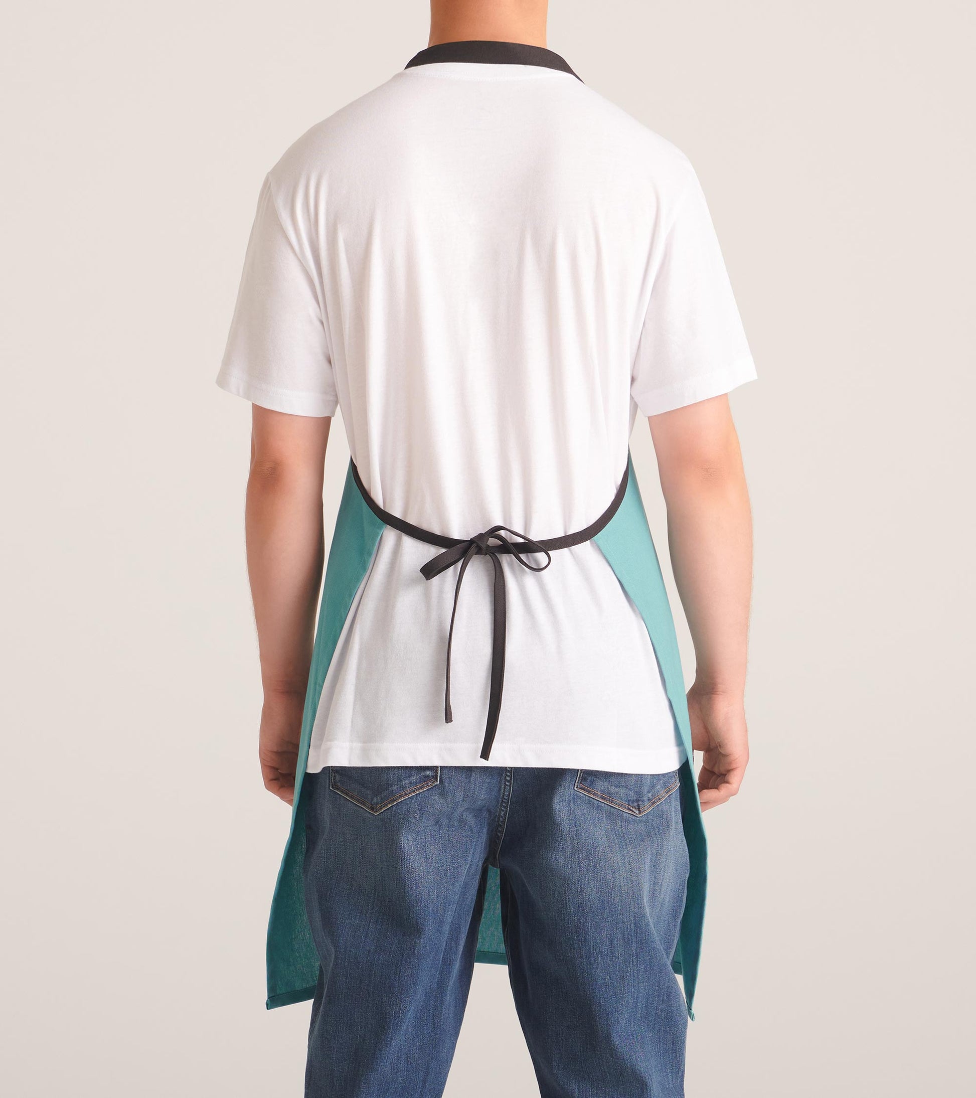 Back view of a white kitchen apron with teal side panels and black neck and waist ties, worn over a white shirt and jeans
