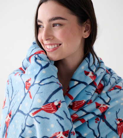 Close-up of a woman wrapped in a light blue fleece blanket with red cardinals, branches, and white snow dots