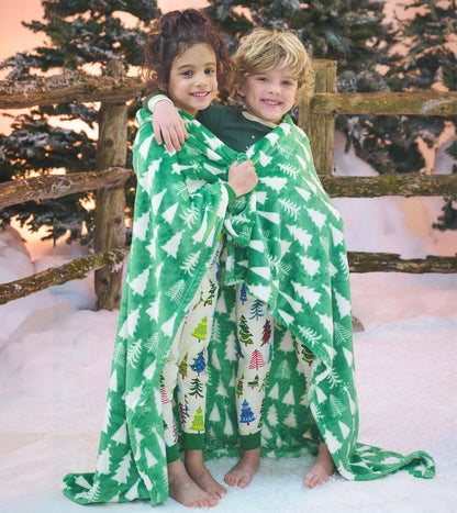 Two children wrapped in a green fleece blanket with white Christmas tree pattern