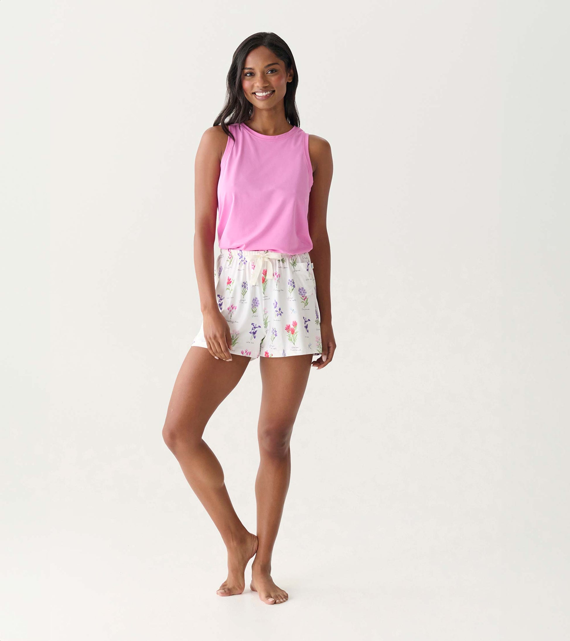 Woman wearing pink sleeveless top and white floral pajama shorts, front view