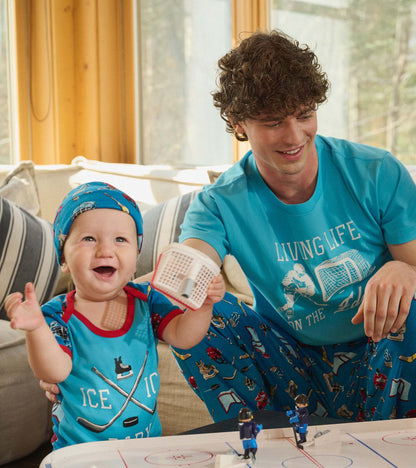 Baby wearing blue hockey print bodysuit and hat, seated beside an adult in matching blue hockey pajamas