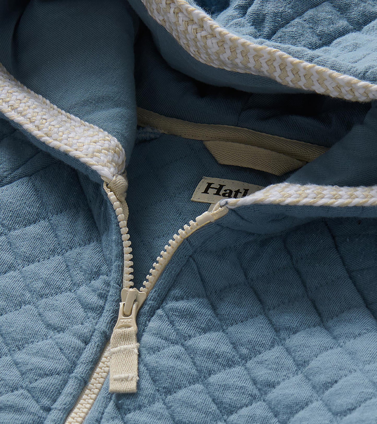 Close-up of faded blue quilted hoodie with cream zipper and braided trim inside the hood