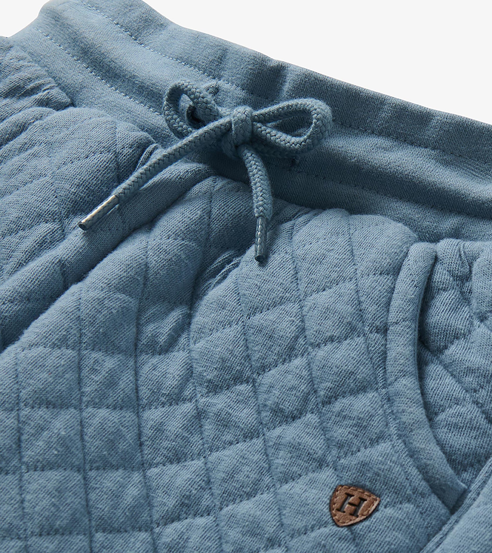 Close-up of faded blue quilted joggers showing the drawstring waistband and small H patch