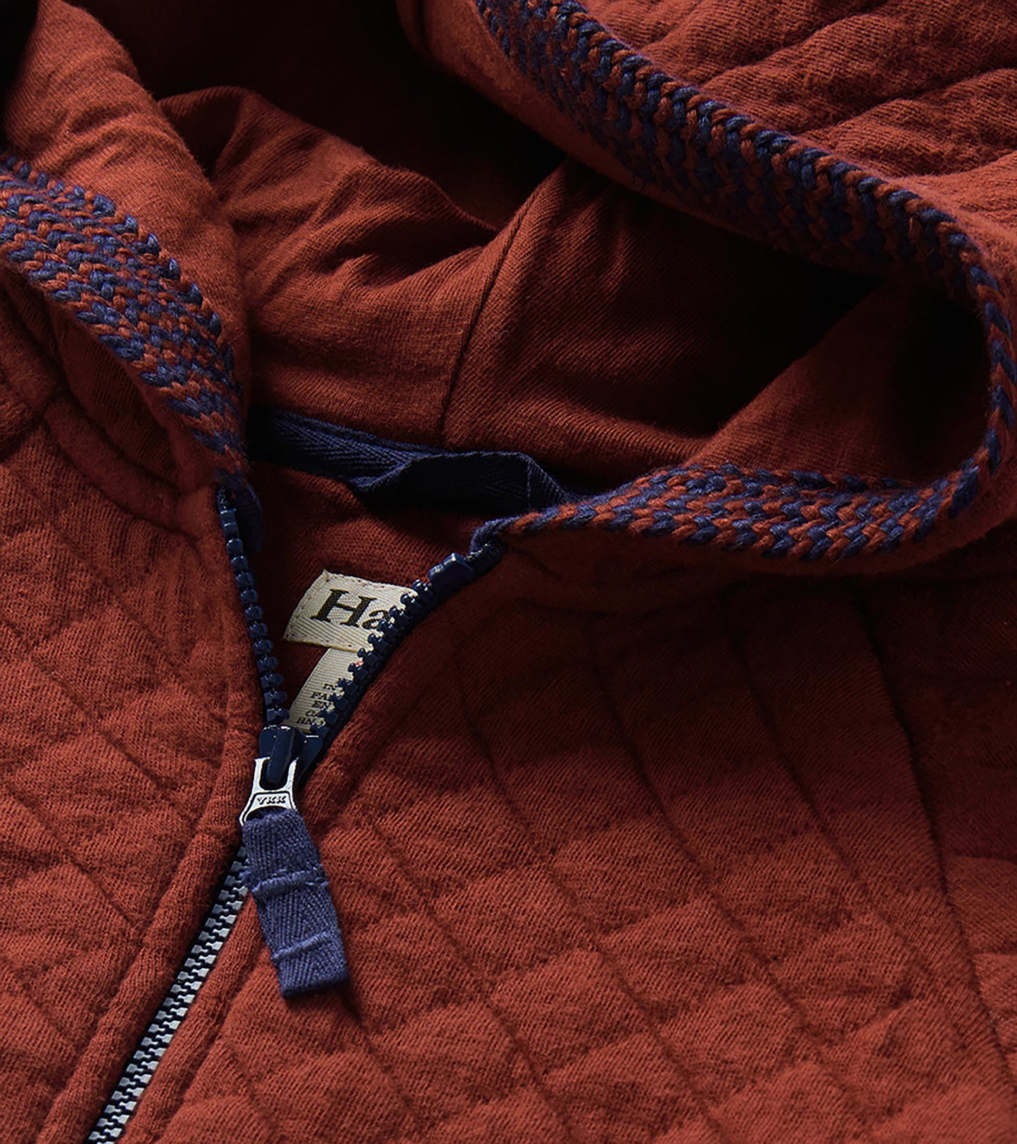 Close-up of madder brown quilted hoodie hood lining, blue zipper, and blue-and-brown trim detail