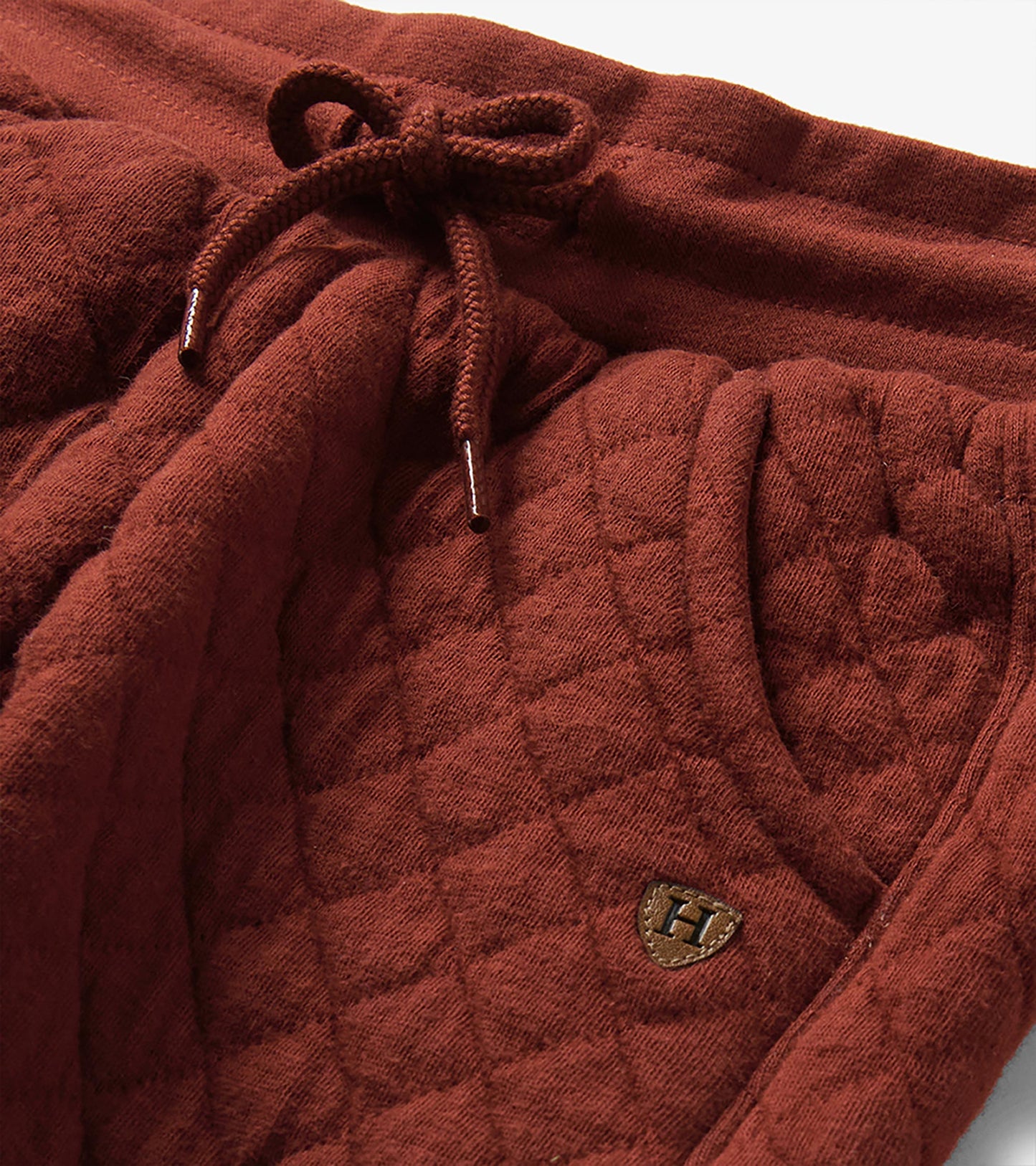 Close-up of madder brown quilted joggers showing elastic drawcord waistband and textured pattern