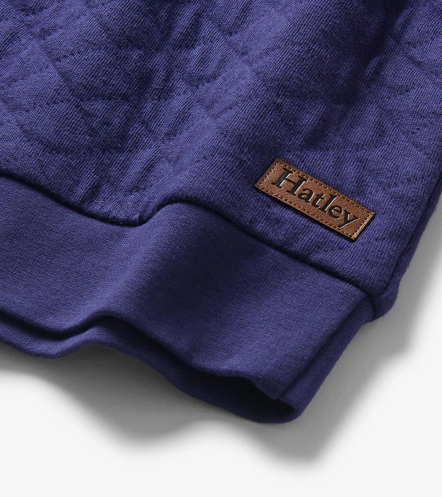 Close-up of the pullover hem with quilted blue fabric, ribbed trim, and visible Hatley logo patch