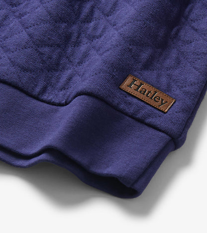 Close-up of the pullover hem with quilted blue fabric, ribbed trim, and visible Hatley logo patch