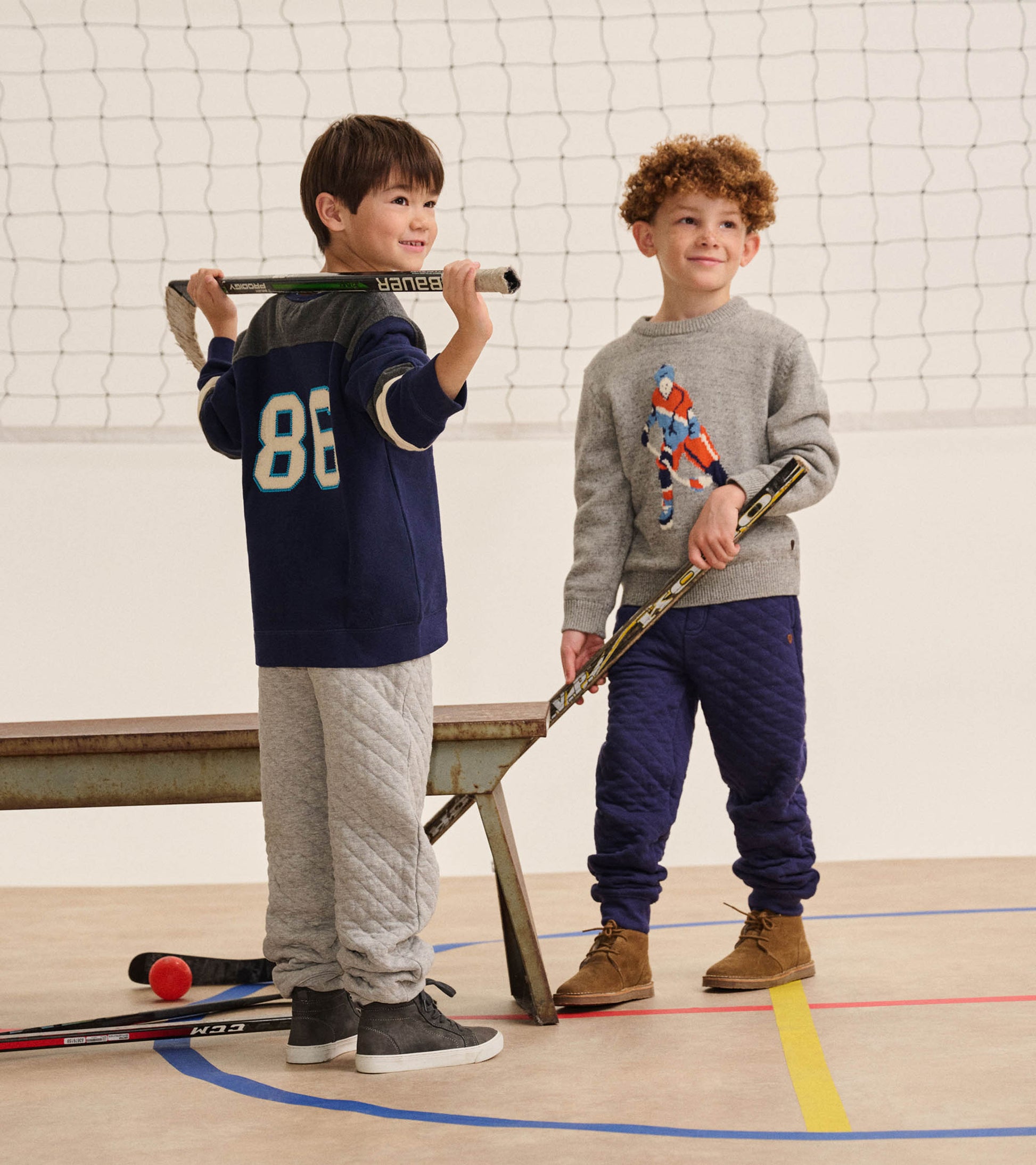 Boy wearing patriot blue quilted joggers in a gym, paired with a gray sweater and brown lace-up boots