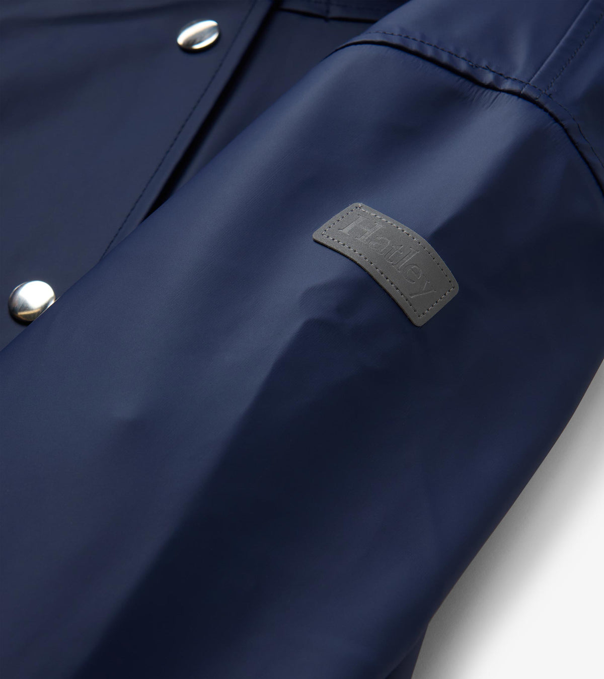 Close-up of patriot blue rain jacket sleeve with gray Hatley logo patch and silver snaps