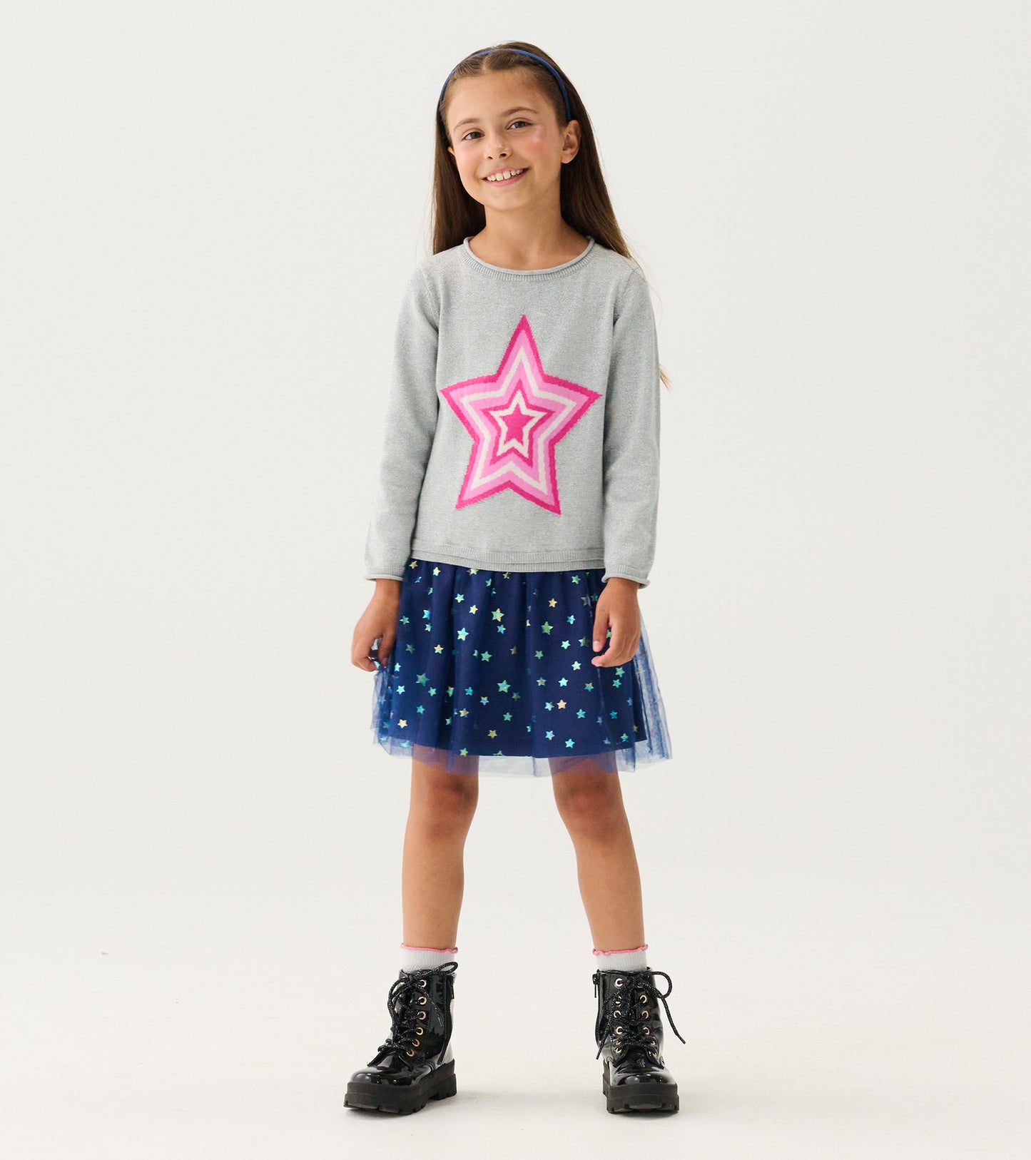 Girl wearing gray sweater dress with pink star and navy star-print tulle skirt, front view