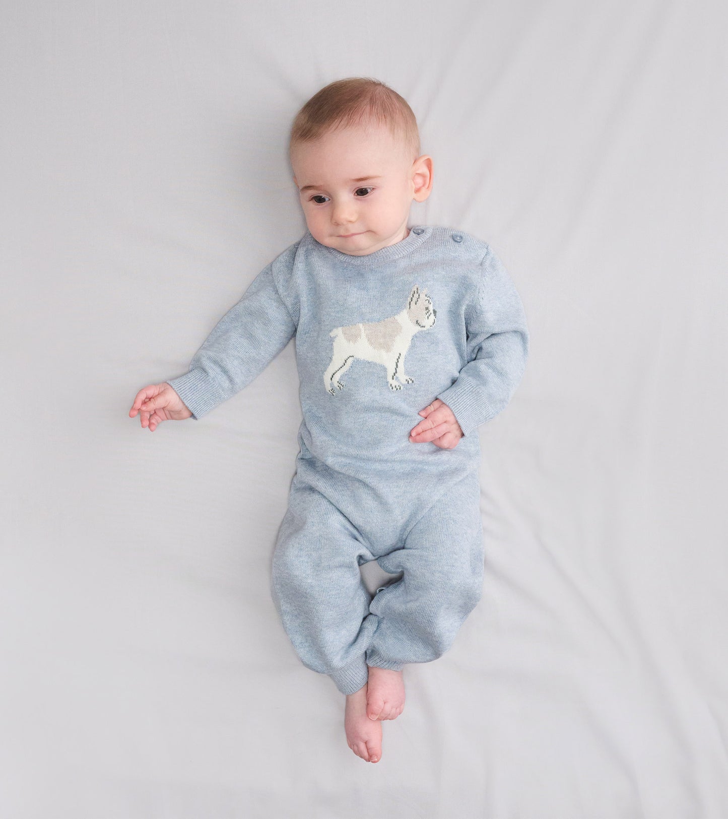 Light blue knit baby romper with a bulldog graphic, long sleeves, and footed legs, shown on a baby lying down