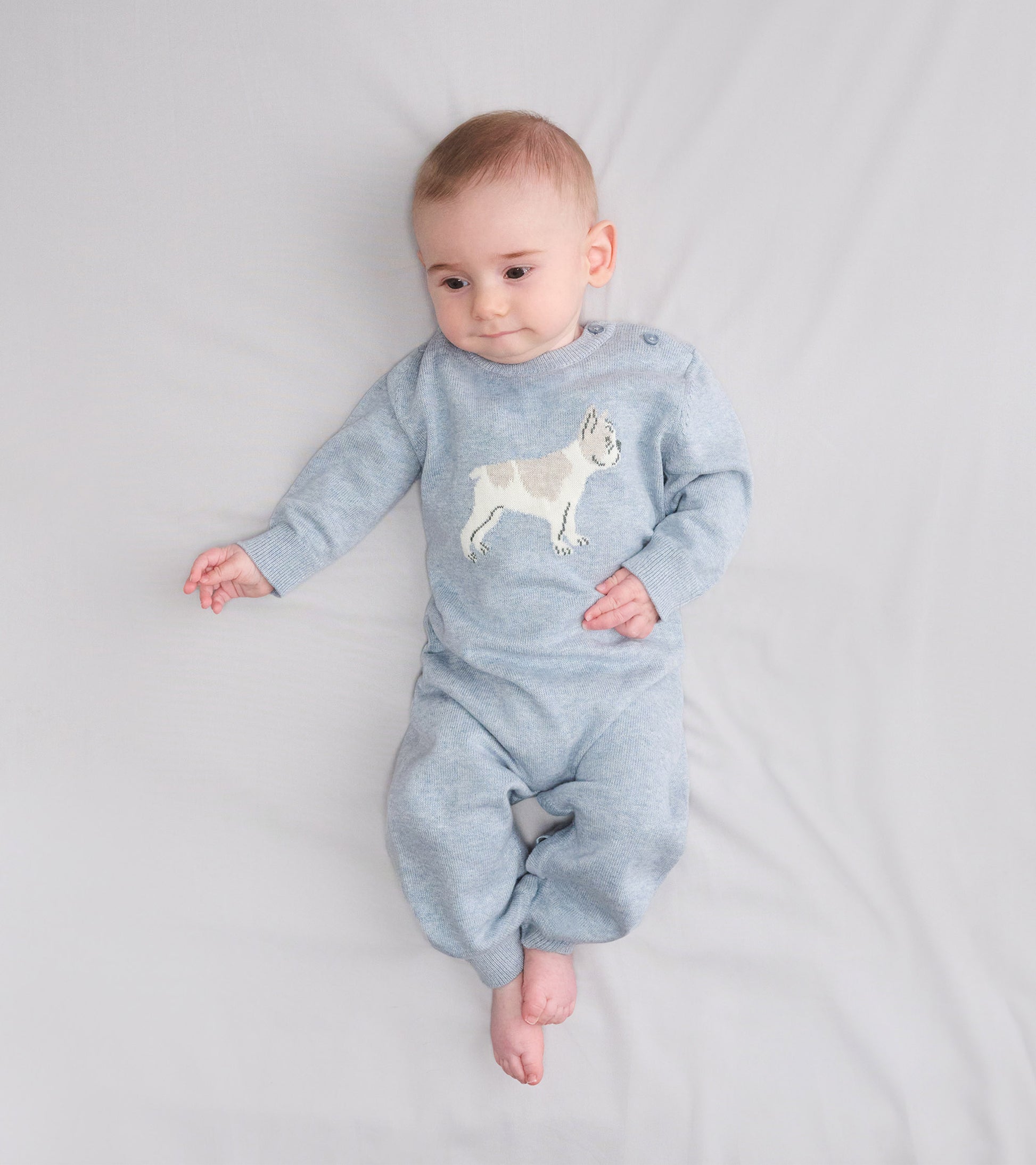 Light blue knit baby romper with a bulldog graphic, long sleeves, and footed legs, shown on a baby lying down