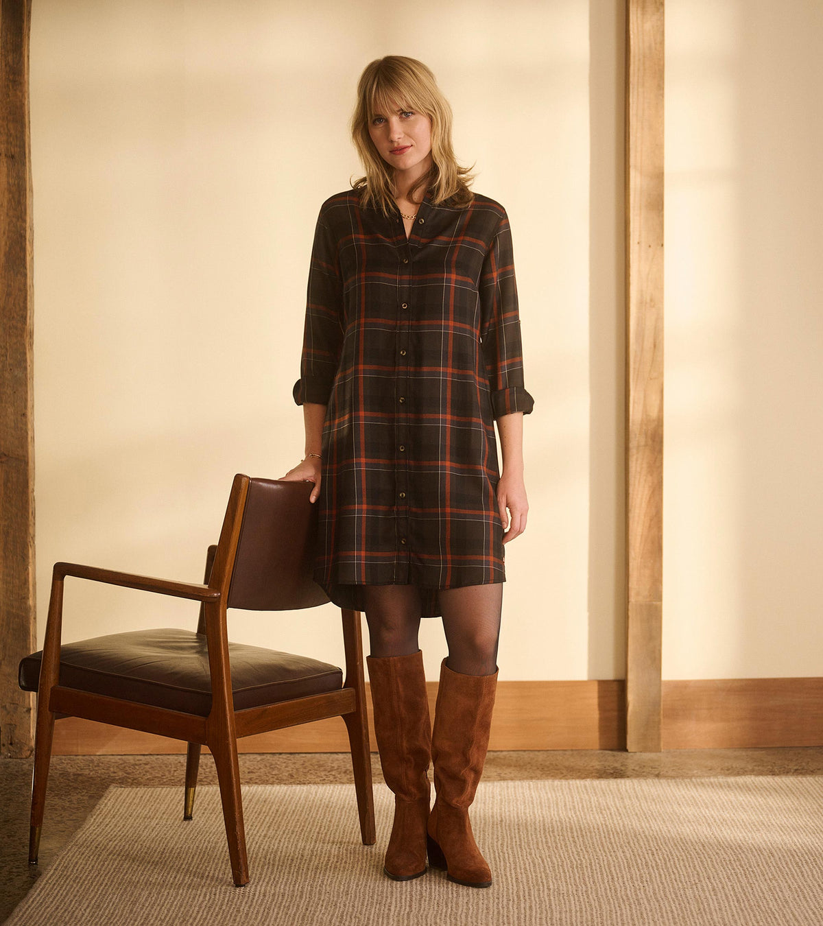 Woman wearing autumn plaid shirt dress with rolled sleeves, shown front view with knee-high brown boots