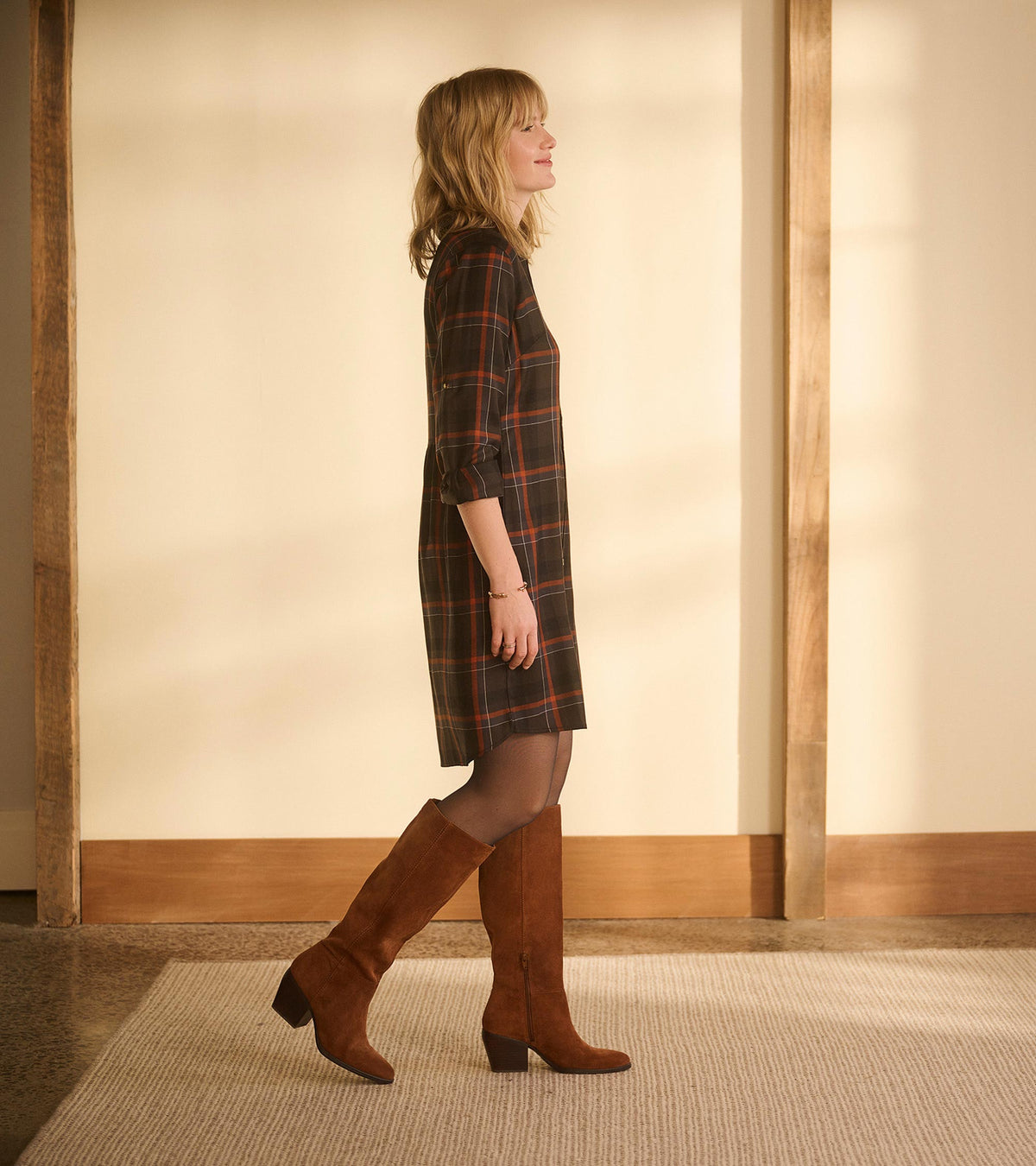 Side profile of autumn plaid shirt dress with rolled sleeves, curved hem, and knee-high brown boots