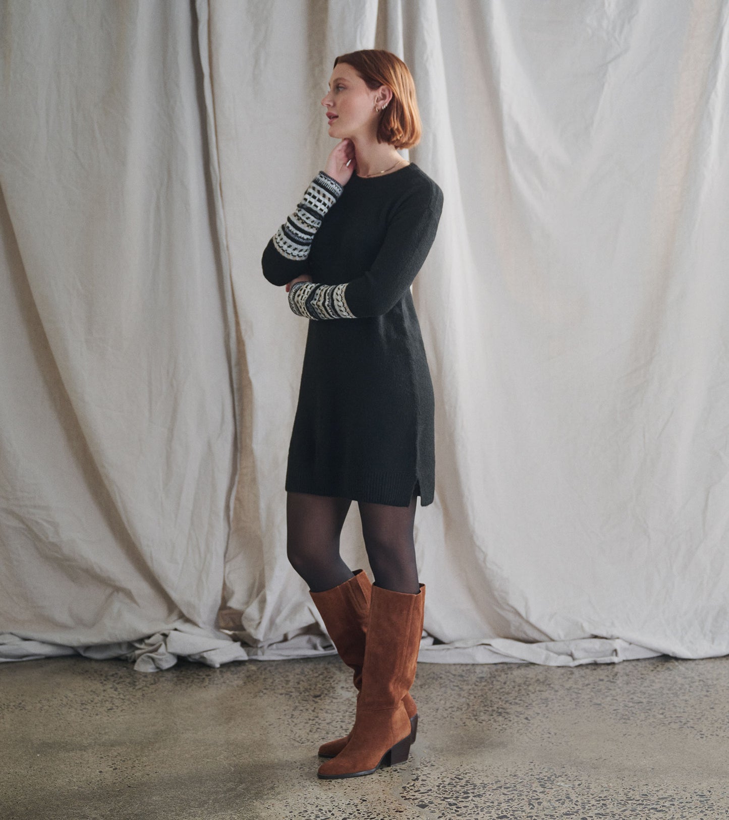 Black knit sweater dress with patterned white-and-black sleeve cuffs, shown on a model in side view.