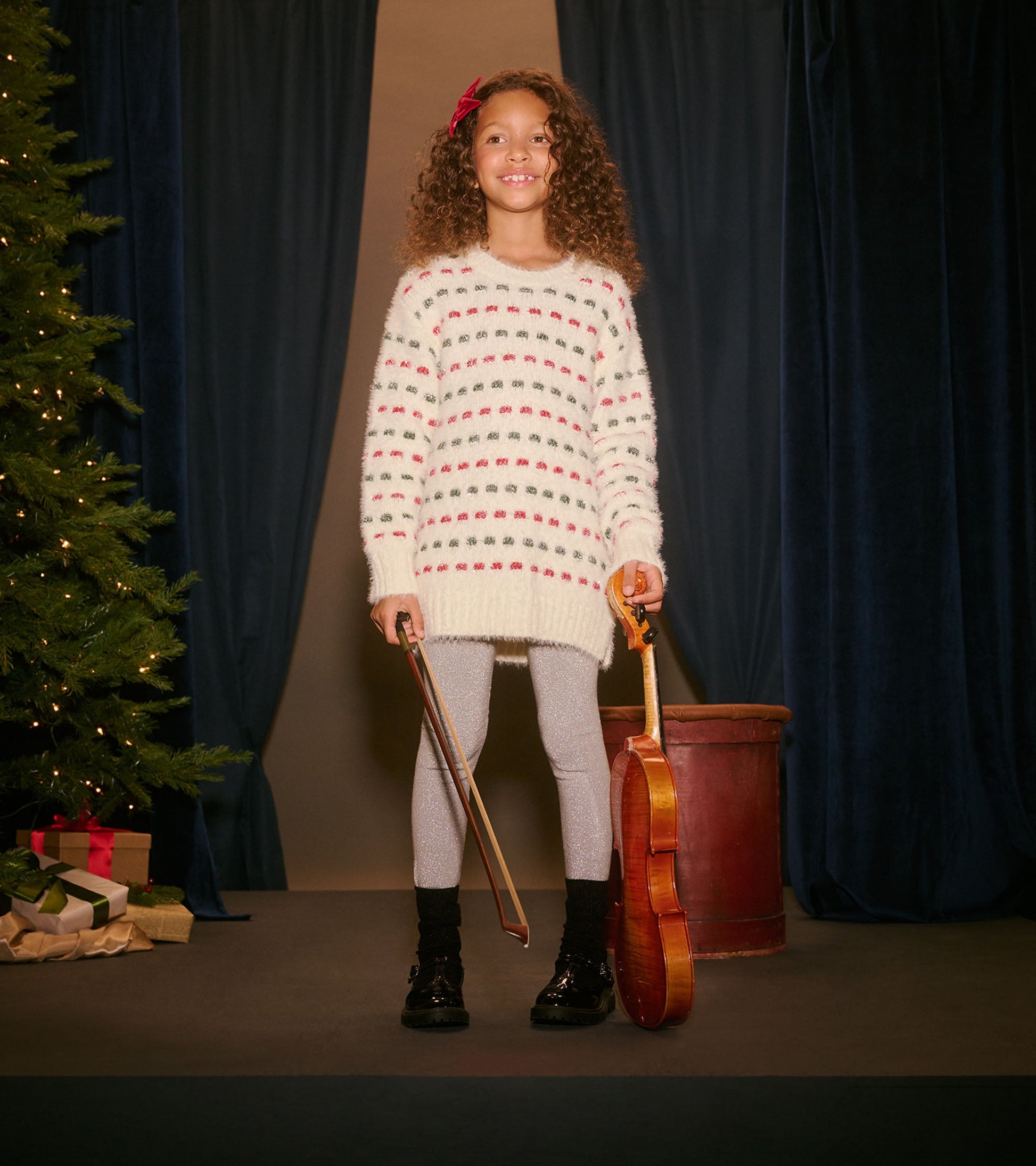 Cream sweater with colorful dots, paired with sparkly leggings and black boots, worn by a girl holding a violin.