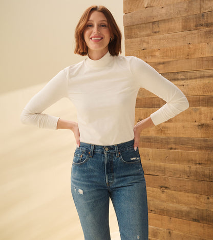 Model wearing cream white mock neck top with long sleeves, front view with hands on hips