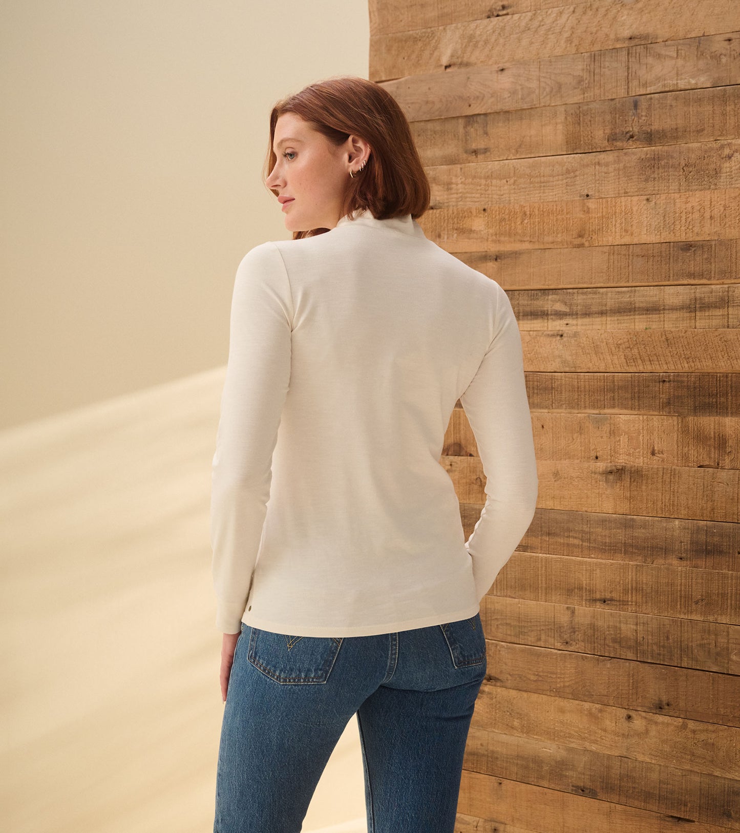 Back view of cream white mock neck top with long sleeves, shown on model