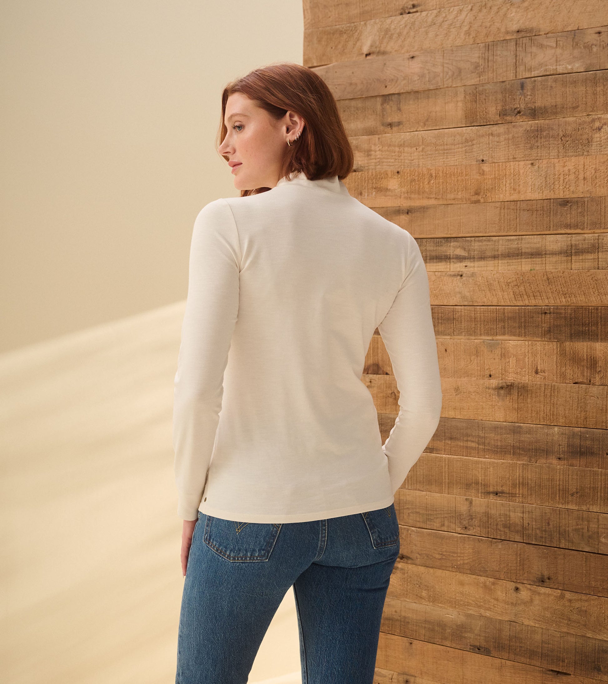 Back view of cream white mock neck top with long sleeves, shown on model