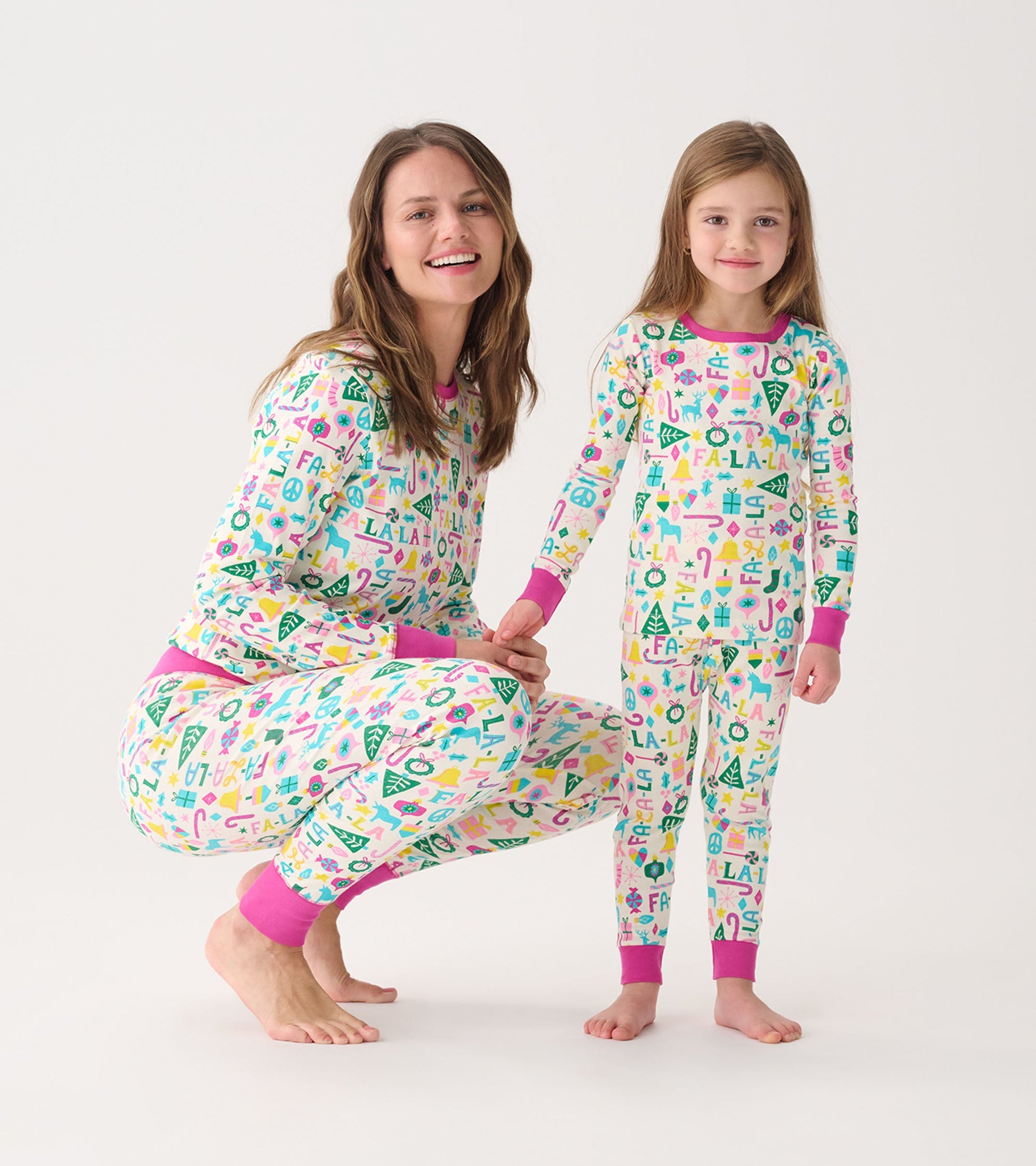 Women's and girl's matching pink pajama set with colorful holiday-themed patterns and contrasting cuffs.