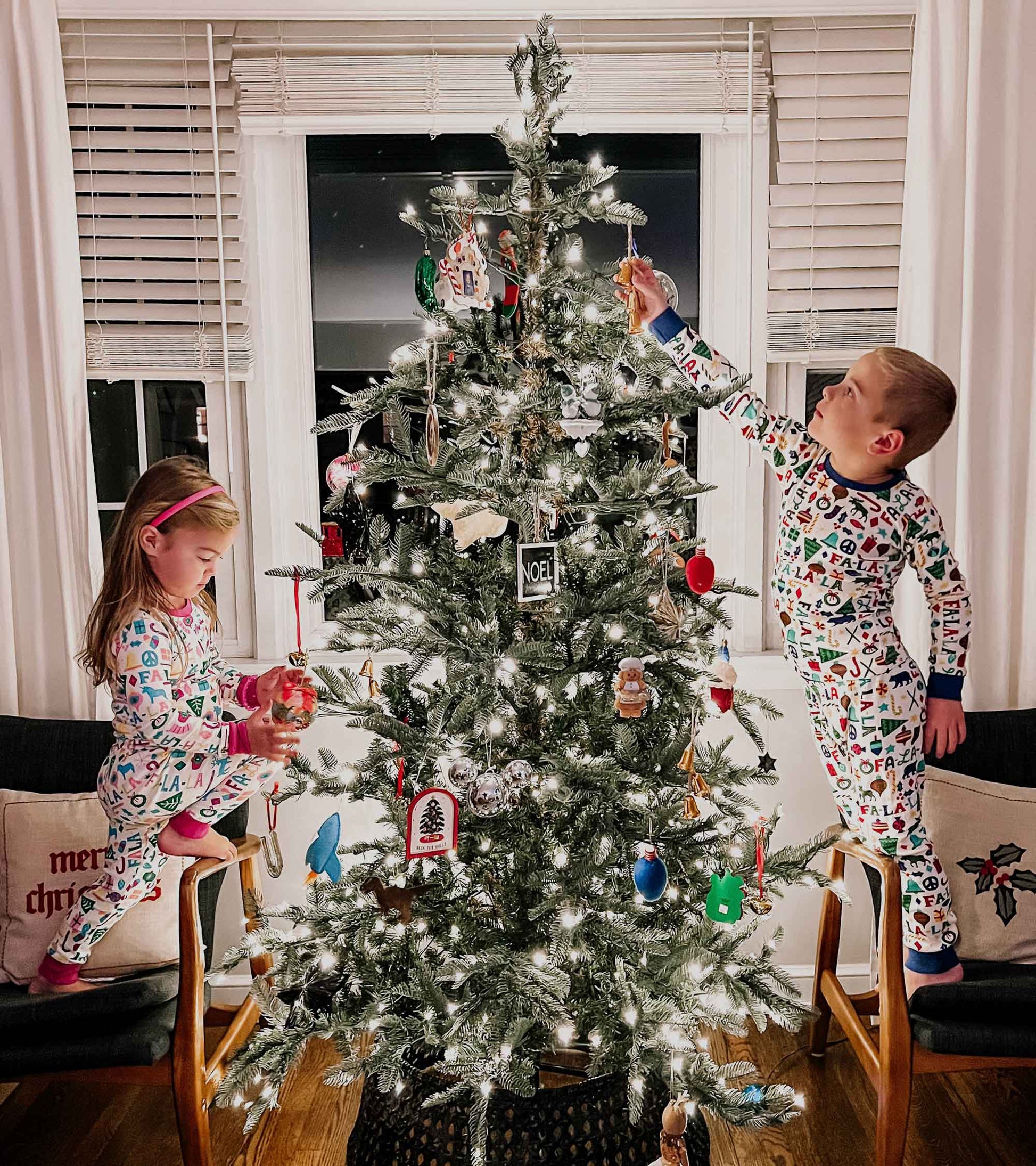 Colorful, festive pajama set featuring holiday-themed patterns, worn by children while decorating a Christmas tree.