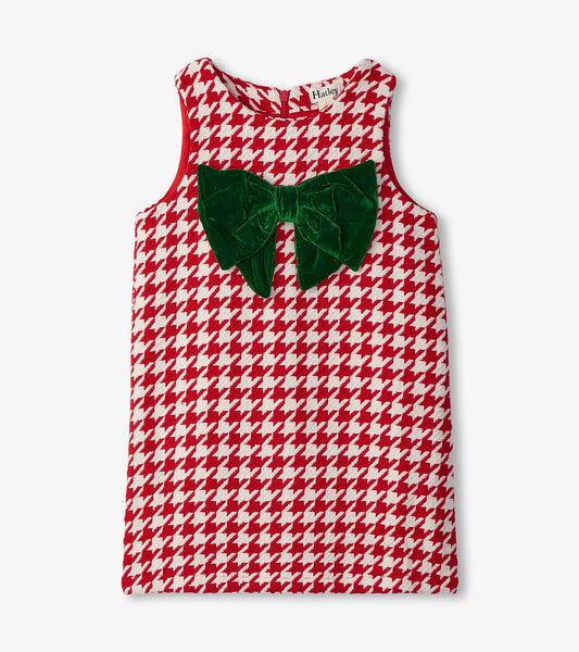 Red and white houndstooth dress featuring a large green velvet bow on the front. Sleeveless design with a round neckline.