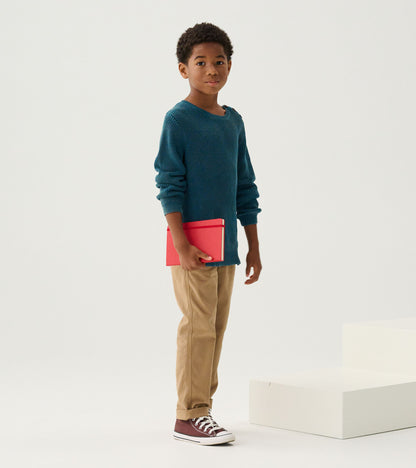Boy in a Moroccan blue knit sweater holding a red notebook, shown in full length