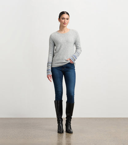 Grey melange sweater with patterned cuffs, crew neck, and relaxed fit, paired with dark jeans and knee-high boots.