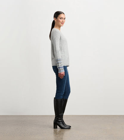 Grey melange sweater with patterned cuffs, featuring a relaxed fit and long sleeves, styled with jeans and knee-high boots.
