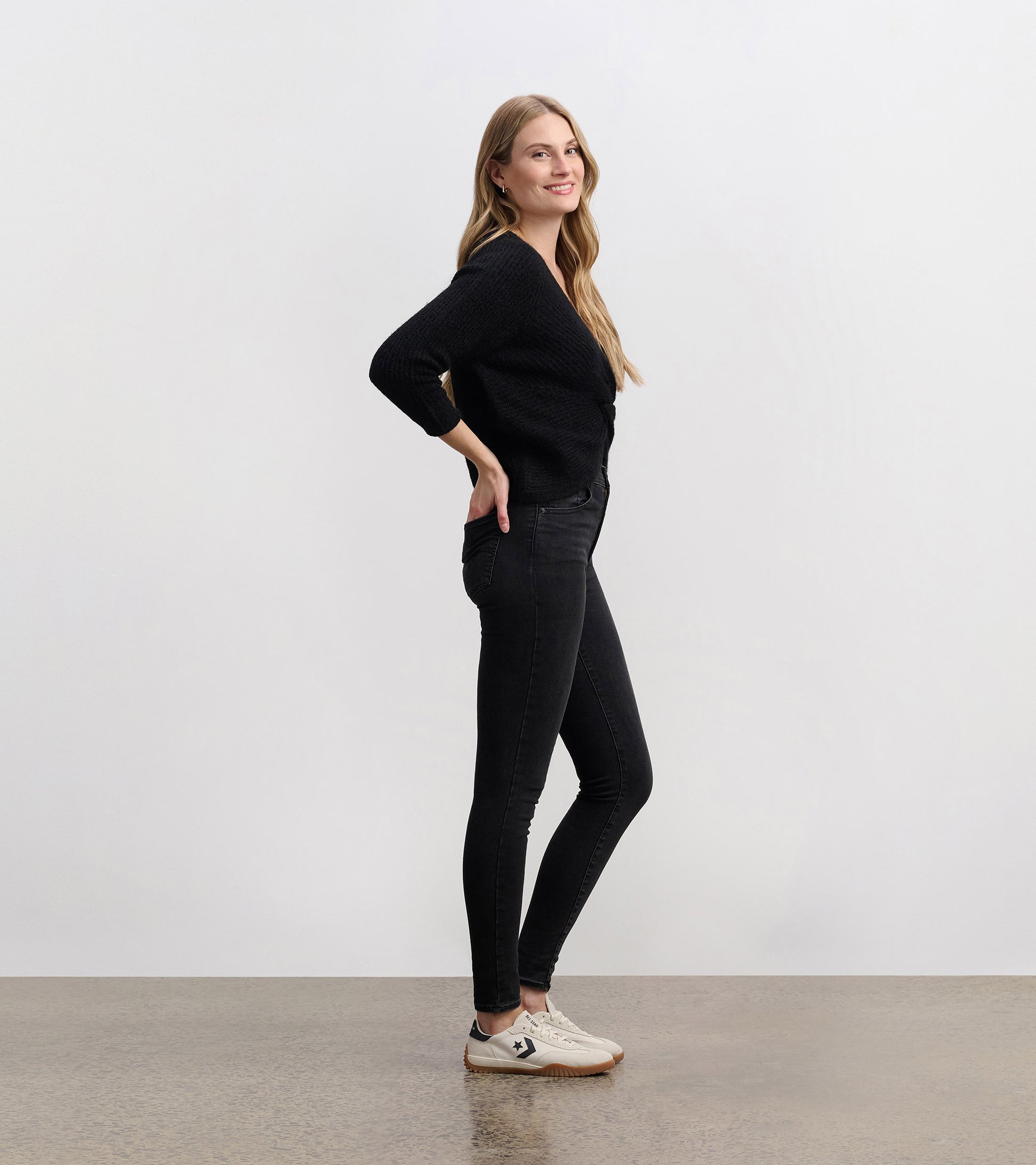 Black crossover sweater with three-quarter sleeves, styled with fitted black jeans and casual sneakers.