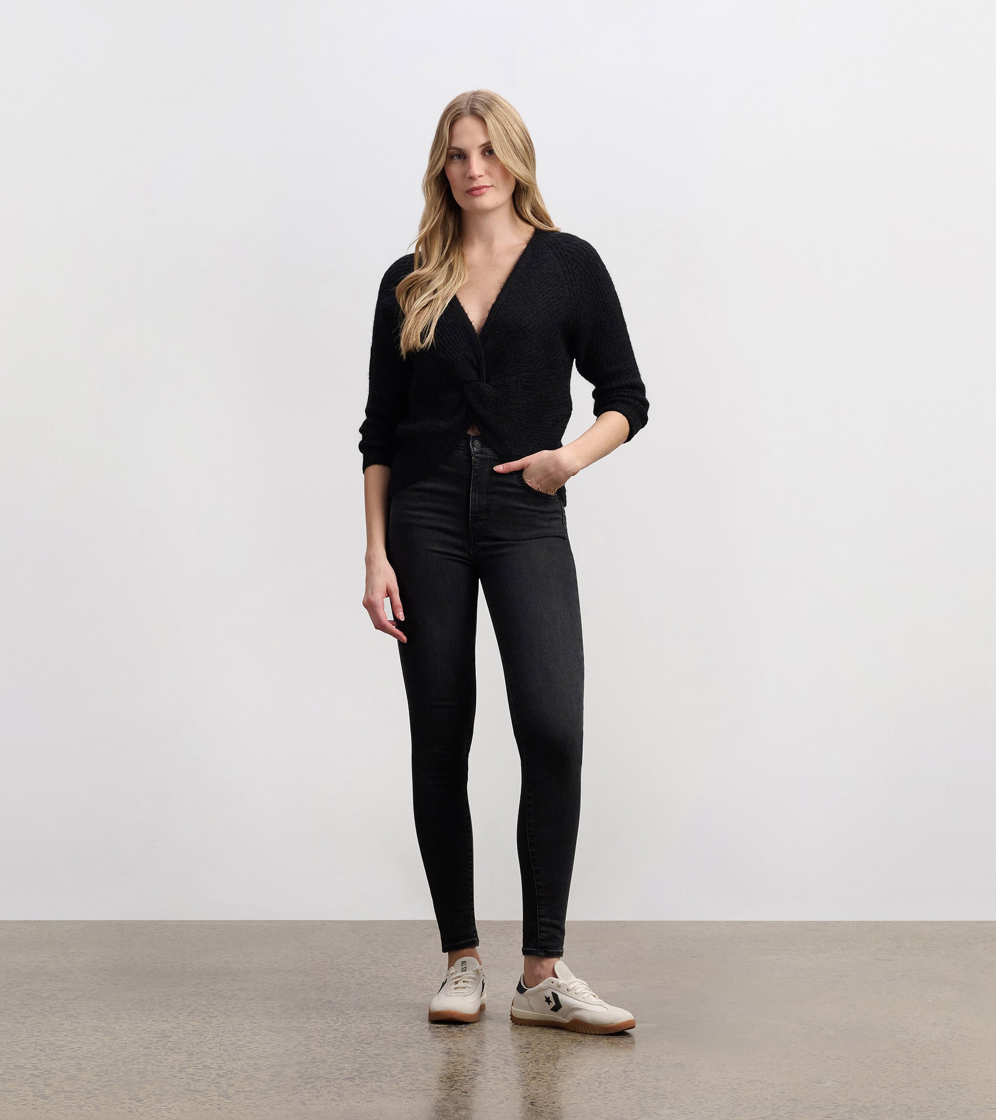Black crossover sweater with a textured finish, featuring a deep V-neck and three-quarter sleeves, styled with skinny jeans.