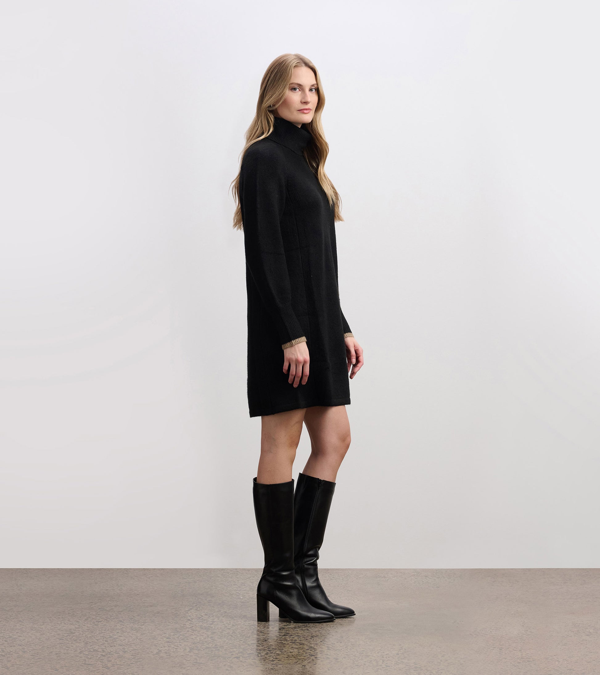 Black swing sweater dress with a high collar and long sleeves, styled with knee-high black boots.