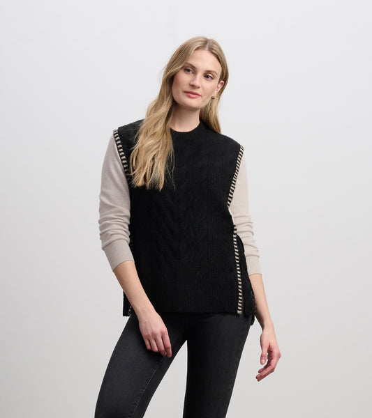 Black side-tie sweater vest with cable knit texture and striped trim, styled over a light long-sleeve top.