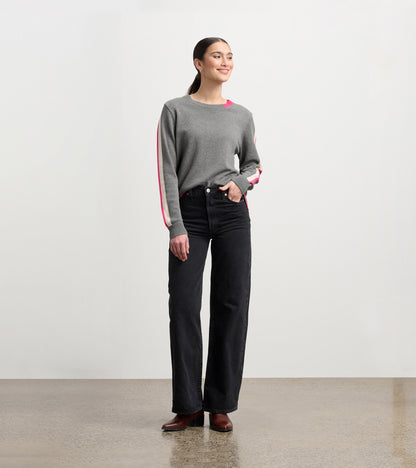 Charcoal sweater with contrast pink trim, long sleeves, and a relaxed fit, styled with high-waisted black jeans.