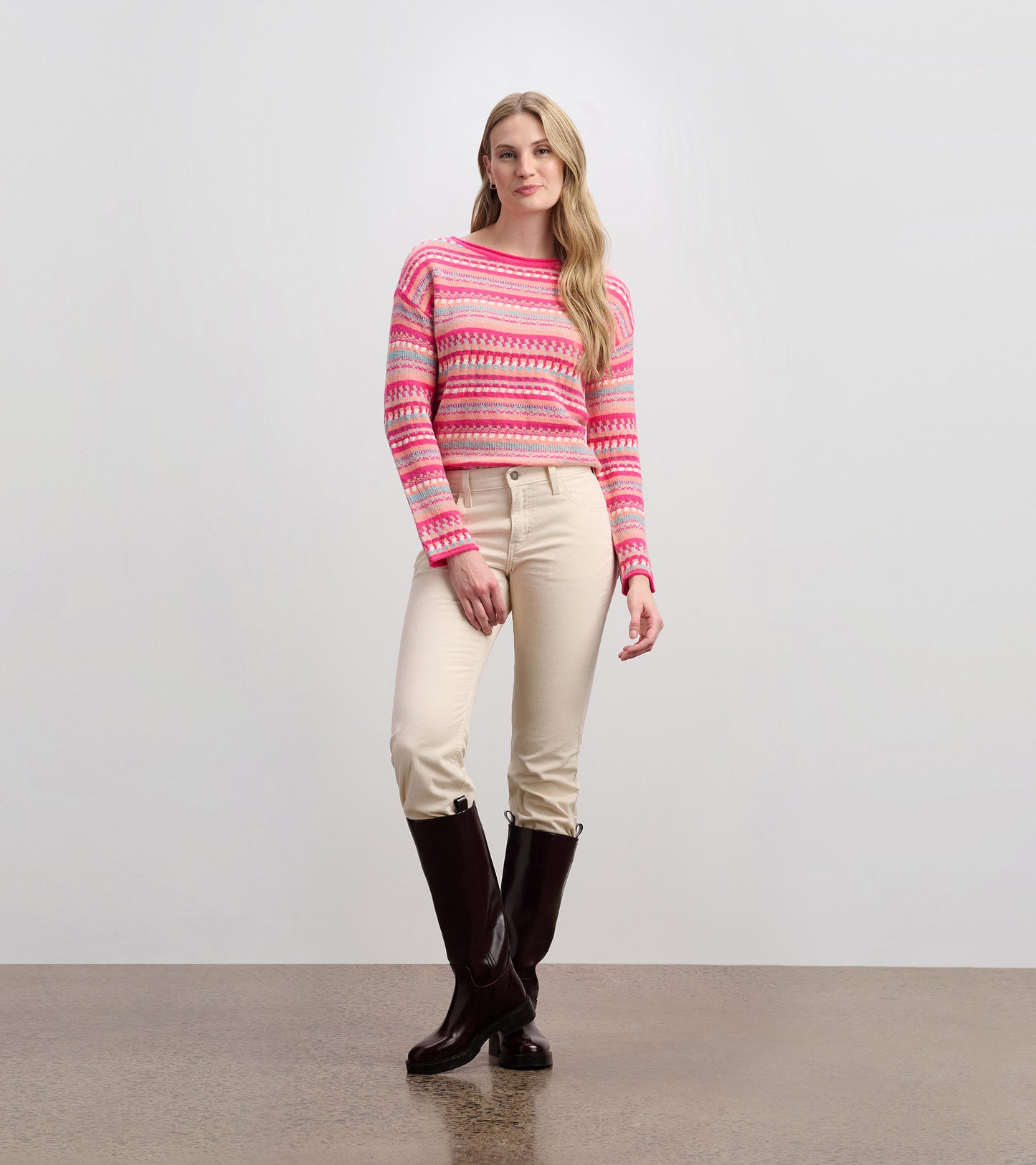 Crochet-style sweater in pink and red hues, featuring a round neckline and long sleeves, paired with light-colored pants.