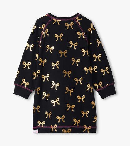 Black sweater dress featuring a gold bow pattern and long sleeves, with contrasting purple stitching.